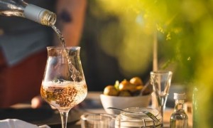 A man pouring a glass of wine under his garden pergola. 